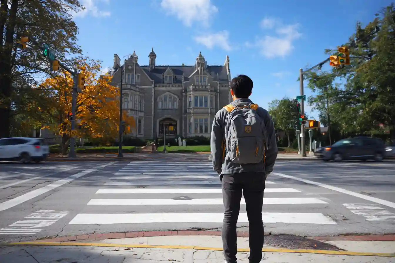 Insert Image alt text hereInternational student standing at a campus crosswalk, looking ahead at a university building, representing forward planning and determination.