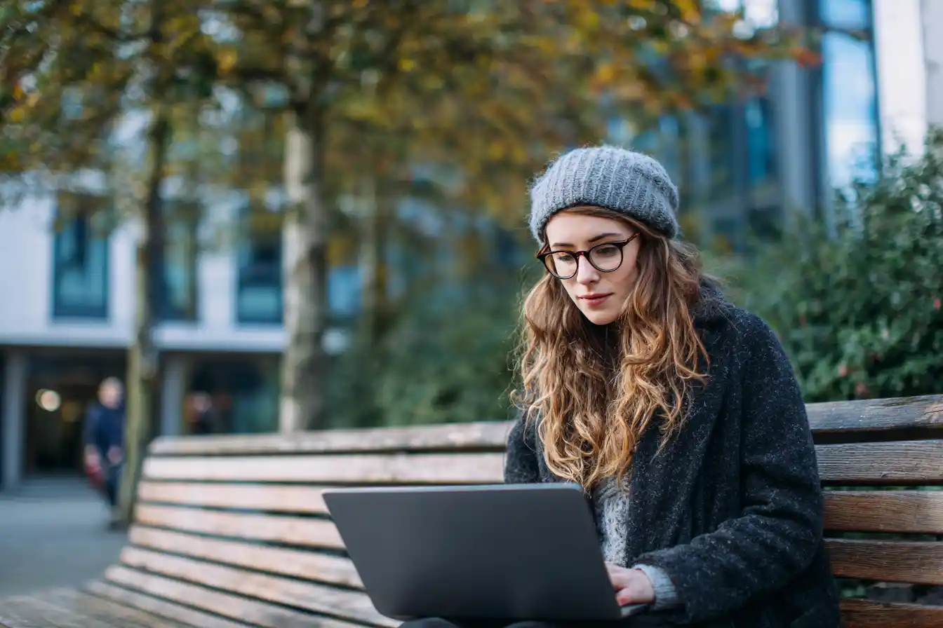 Insert Image alt text hereInternational postgraduate student sitting at an outdoor campus bench, reading a loan approval email on their phone with a look of relief and focus.