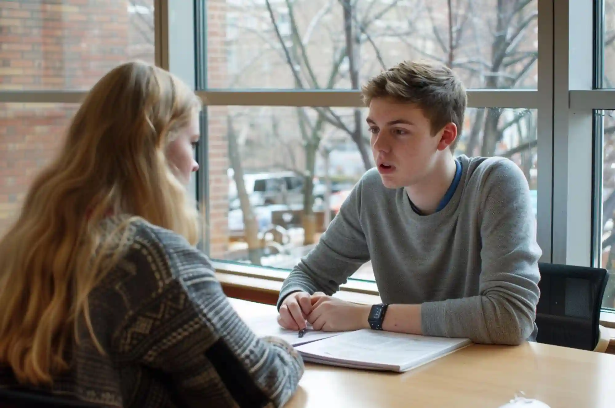 Inside a student lounge, a young adult practices interview questions with a friend.