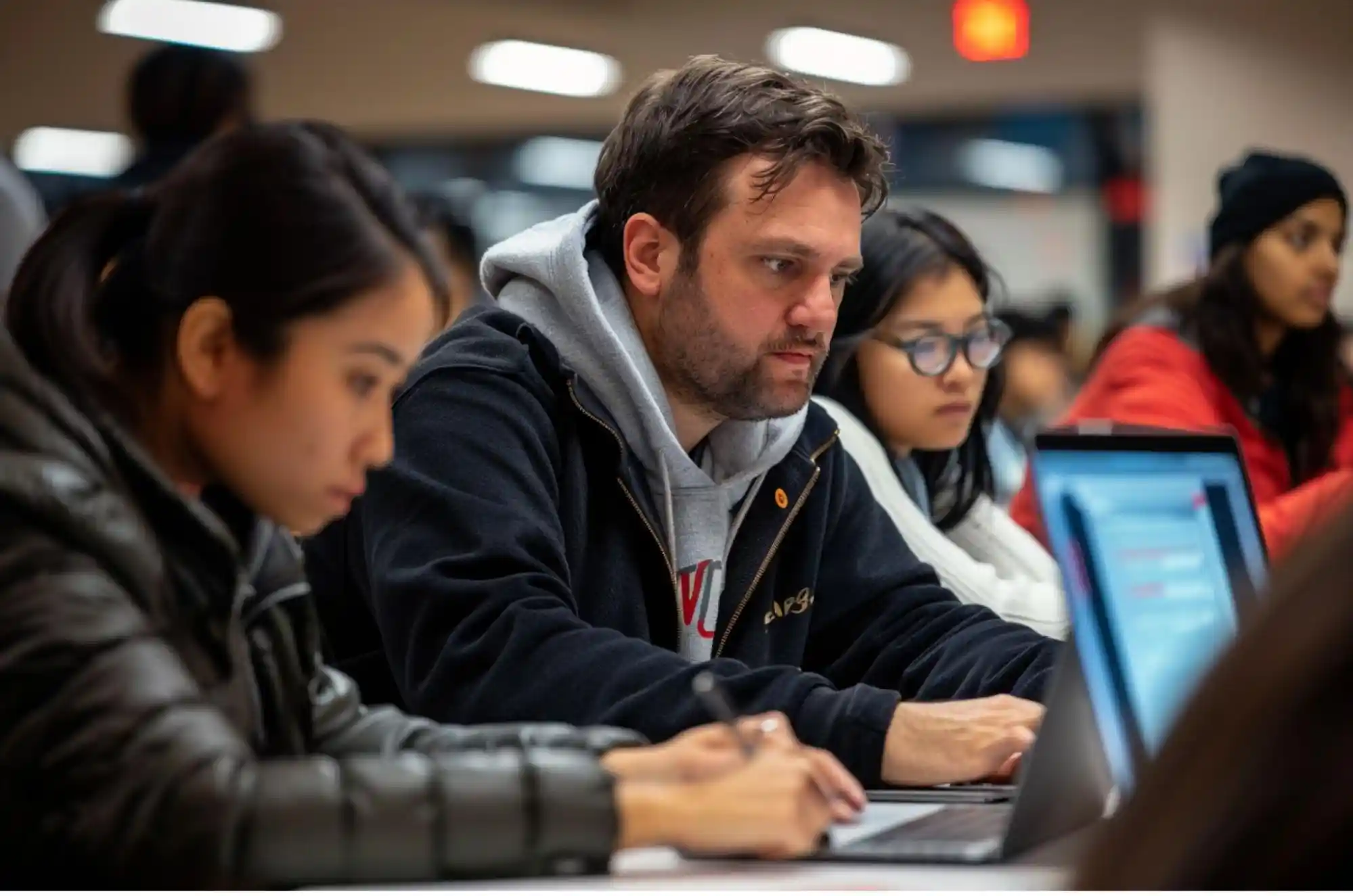 International Students are coding on laptops with a professor guiding them.