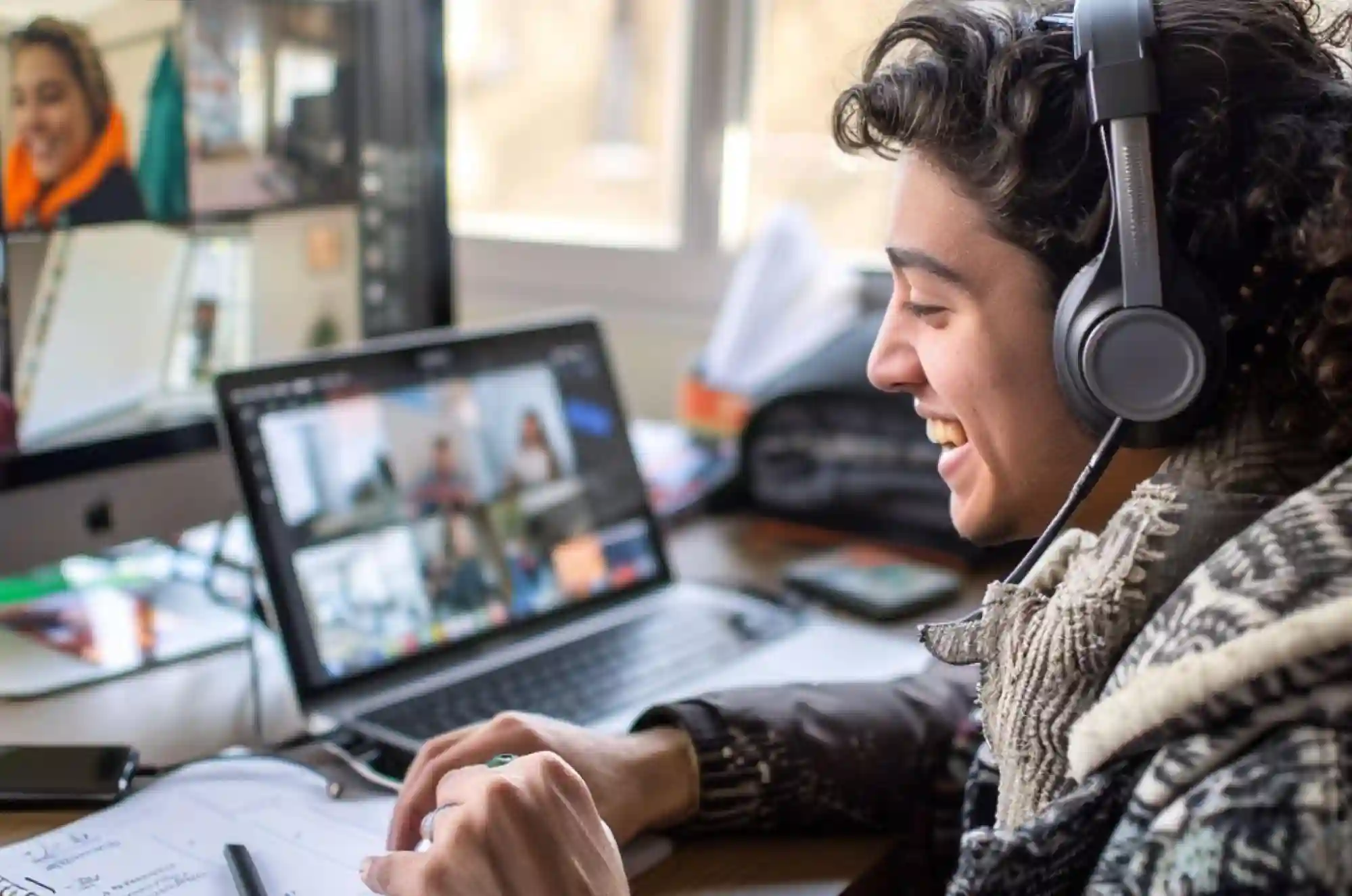 The student wears headphones and smiles at the screen,