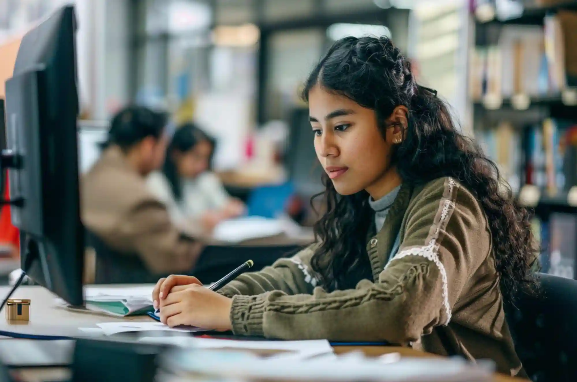 A young international student is working at a computer in a collaborative office setting