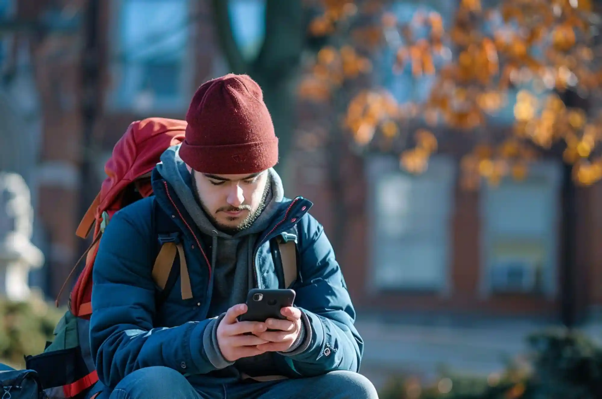 A student reviews their account on a phone banking app while seated outside on campus.