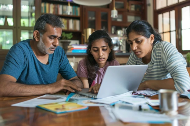 A family in Hyderabad gathers around a dining table covered with university brochures, cost of attendance worksheets and loan approval documents