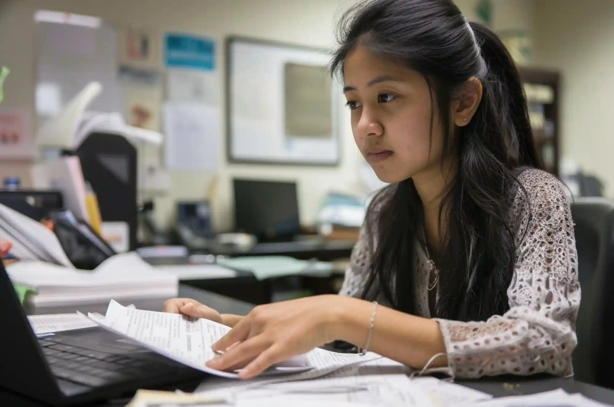 A Nepali student is focused on a laptop with test papers and academic material, representing the hard work required for international students pursuing opportunities like OPT.
